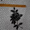 Tela flamenca blanca con pequeños lunares negros y siluetas de flores negras grandes estampadas, ideal para trajes de flamenca.