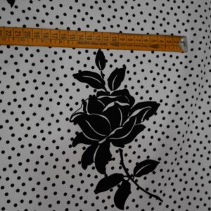 Tela flamenca blanca con pequeños lunares negros y siluetas de flores negras grandes estampadas, ideal para trajes de flamenca.